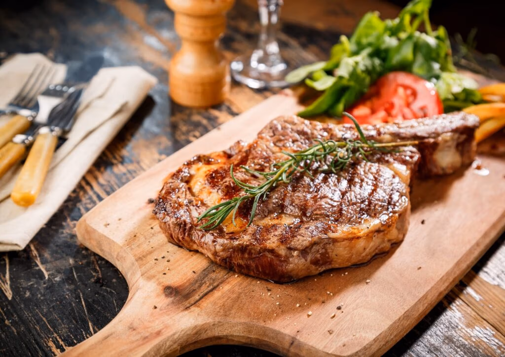 Ein frisch gebratenes Stake auf einem Holzbrett mit einer Tomatenscheiben und Salat als Dekoration.